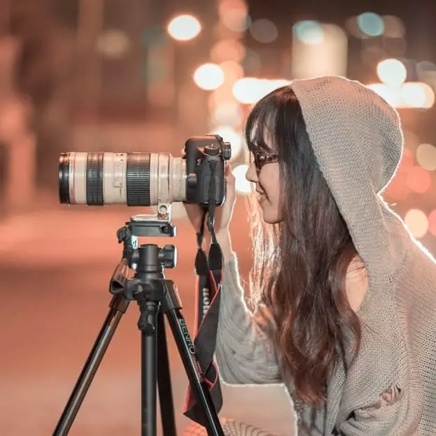 Une image montrant une femme de profil regardant dans l'objectif d'un appareil photo posé sur trépied
