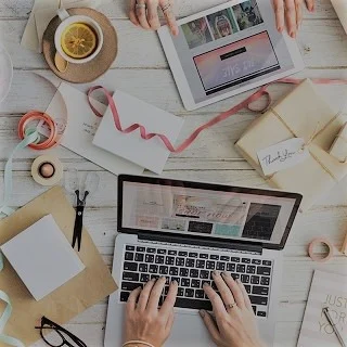 Un bureau en désordes avec des mains tapans sur un ordinateur, une tasse a café est à coté